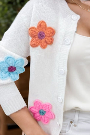 White textured knit cardigan with embroidered flowers in orange, blue, and pink.
