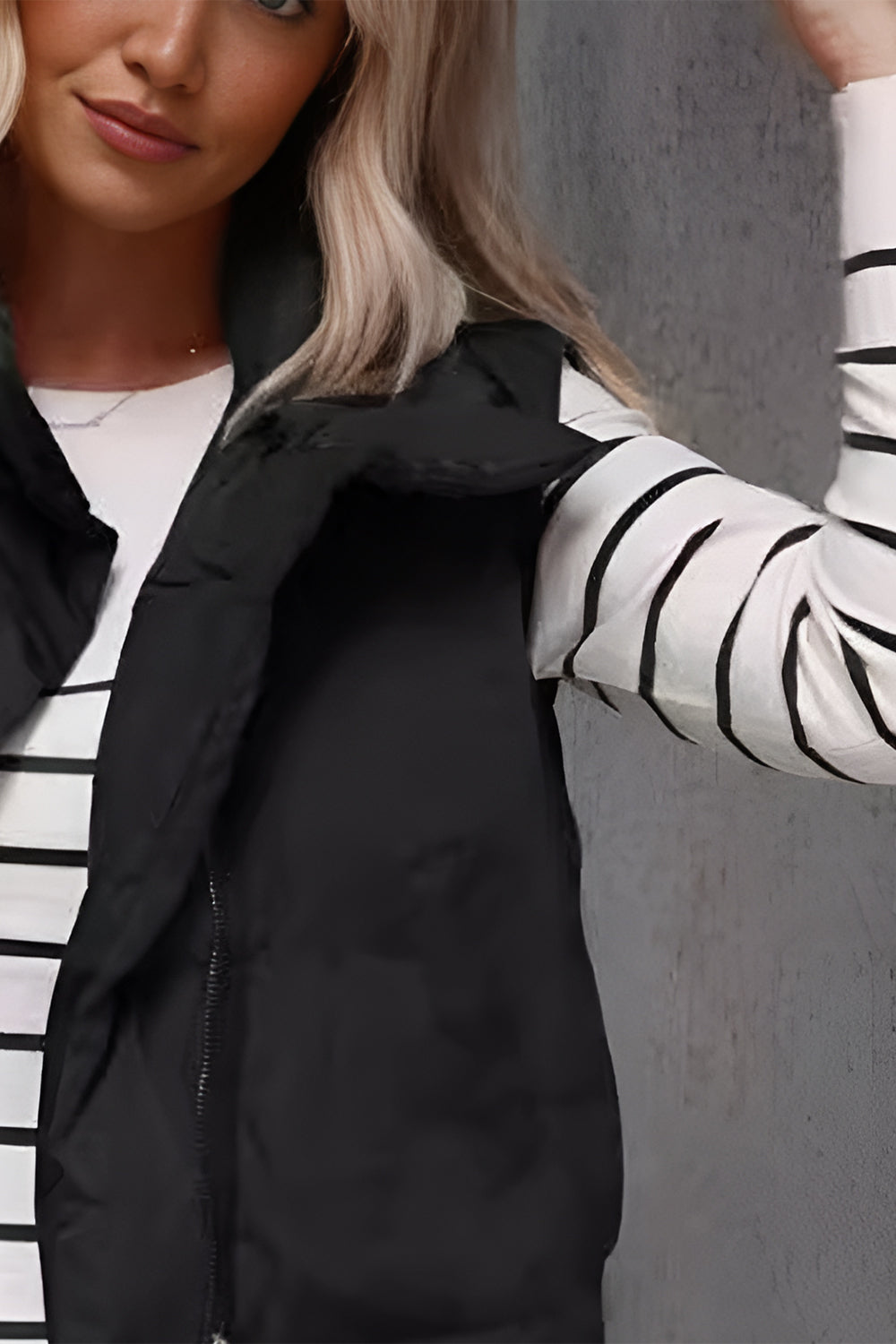 Black padded stand collar vest with zipper closure, styled with a striped long-sleeve shirt.
