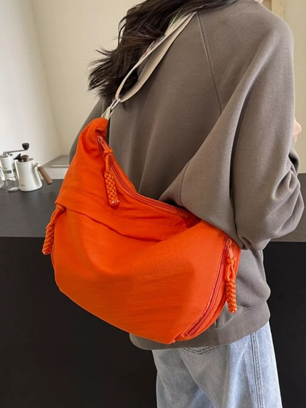 Orange woven strap small crossbody bag with braided zipper pulls.