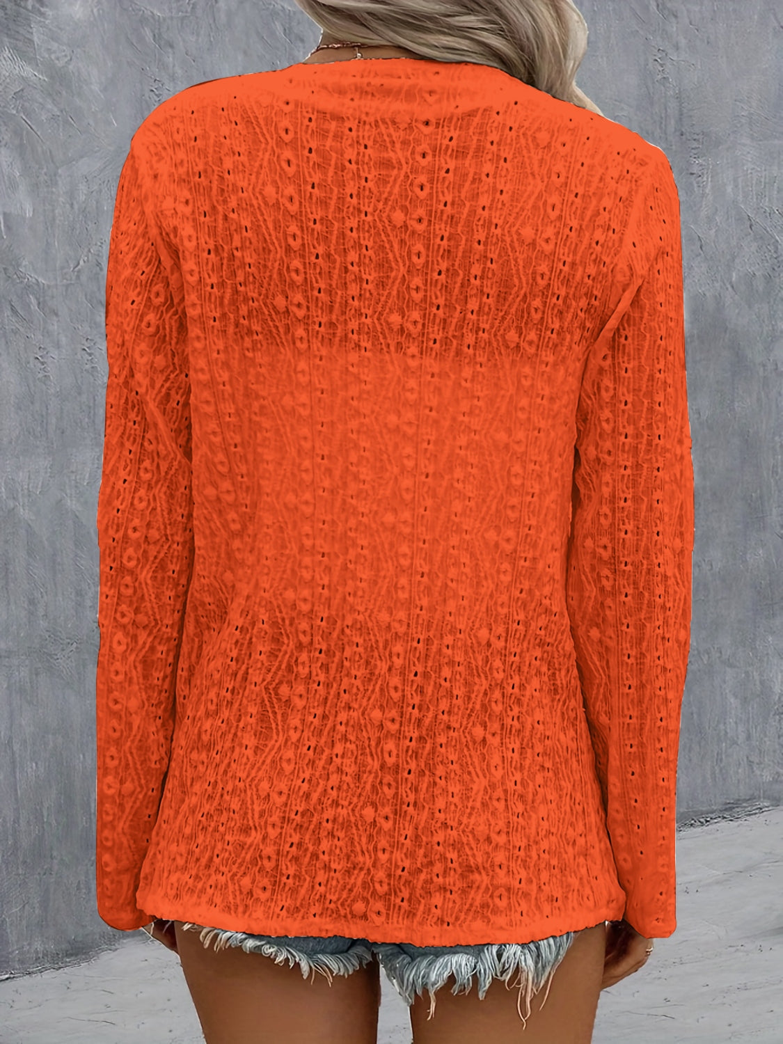 Orange open-weave long sleeve cardigan with a draped front and intricate pattern.