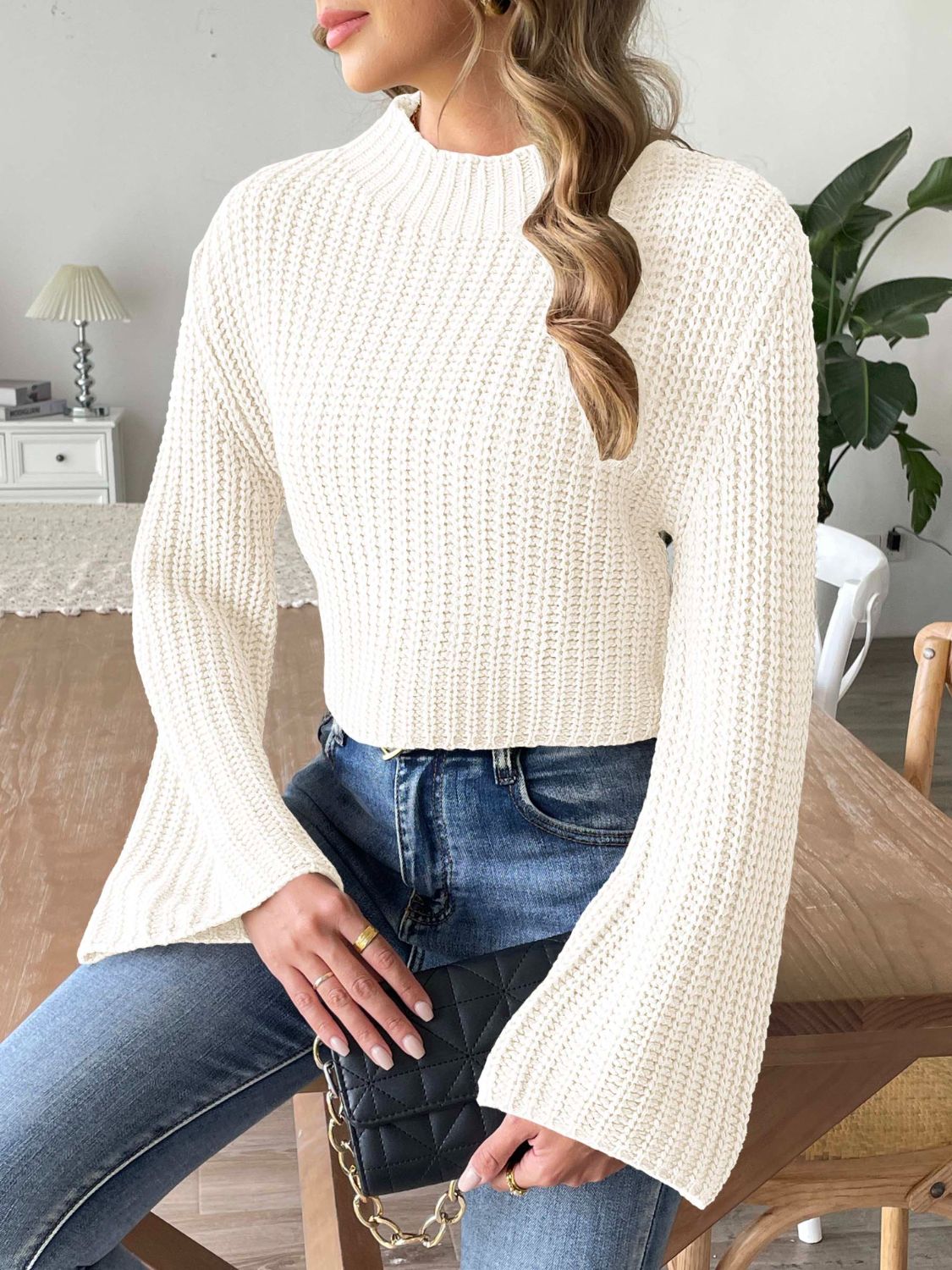 White ribbed crop sweater with bell sleeves and mock neck, styled with jeans and a black clutch.