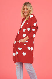 Red acrylic longline cardigan with white heart motif and pockets.