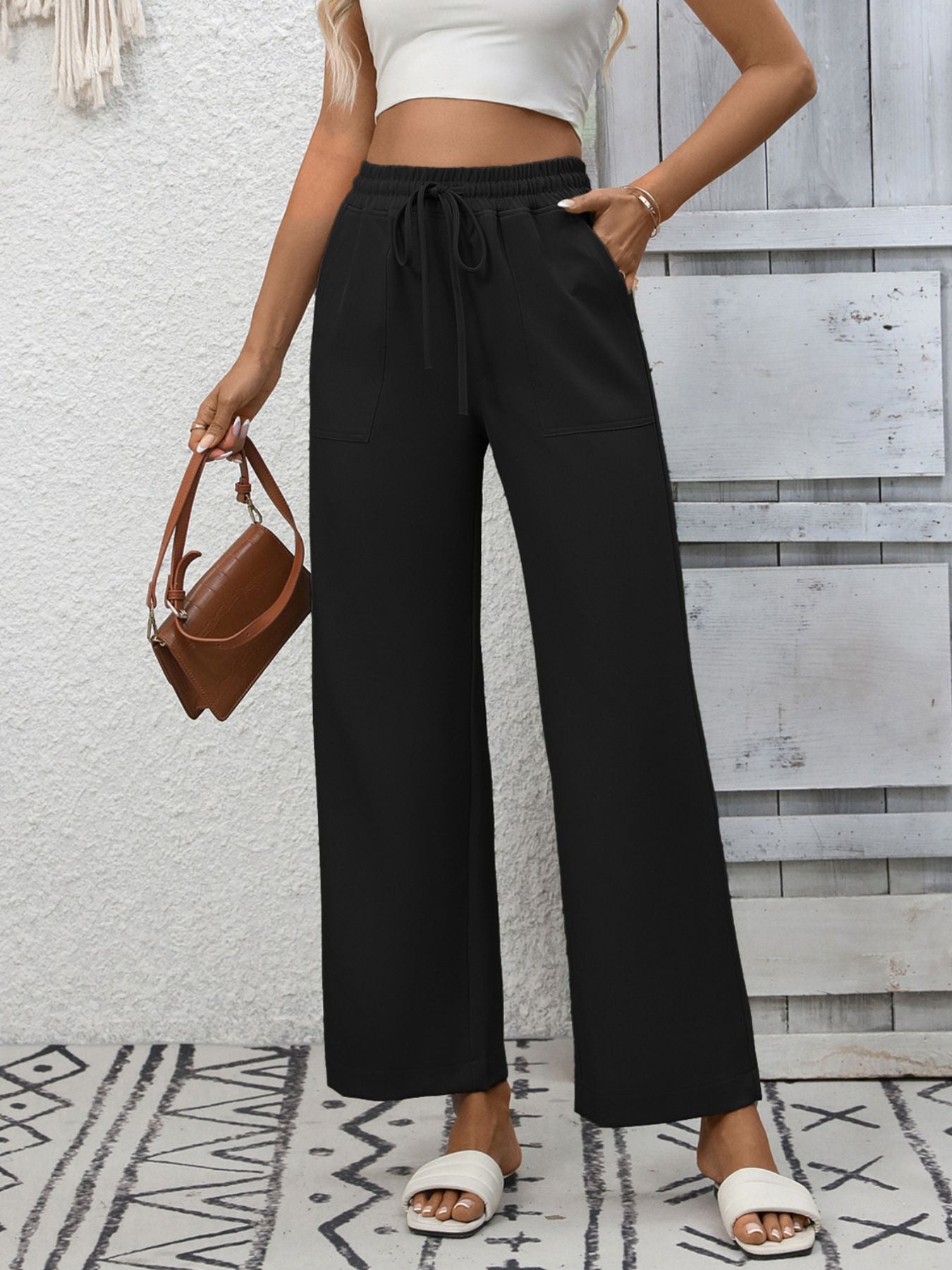 Black relaxed drawstring wide-leg pants with pockets, styled with a white crop top and brown bag.