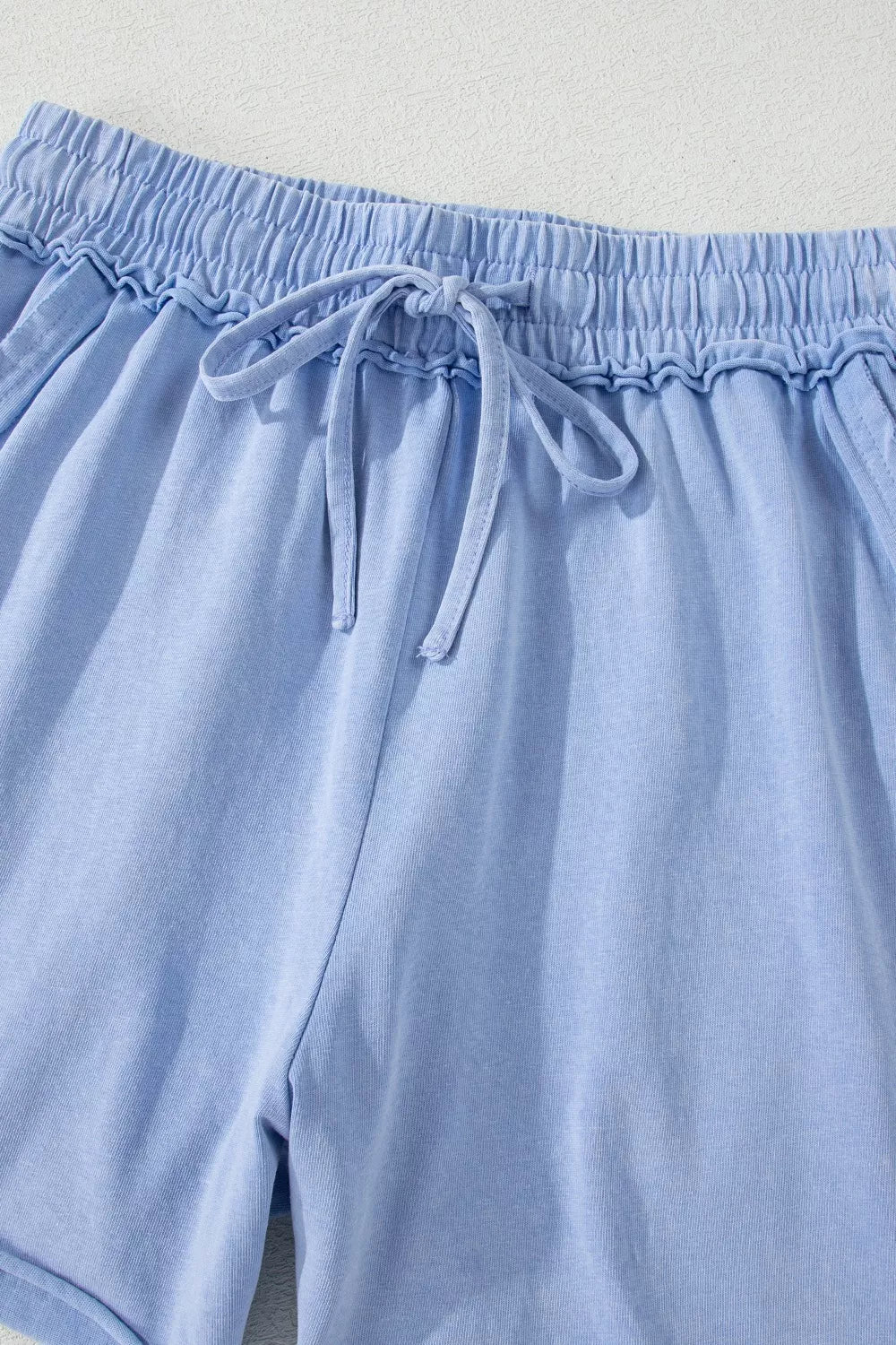 Light blue acid-washed cotton drawstring shorts with pockets and elastic waistband.