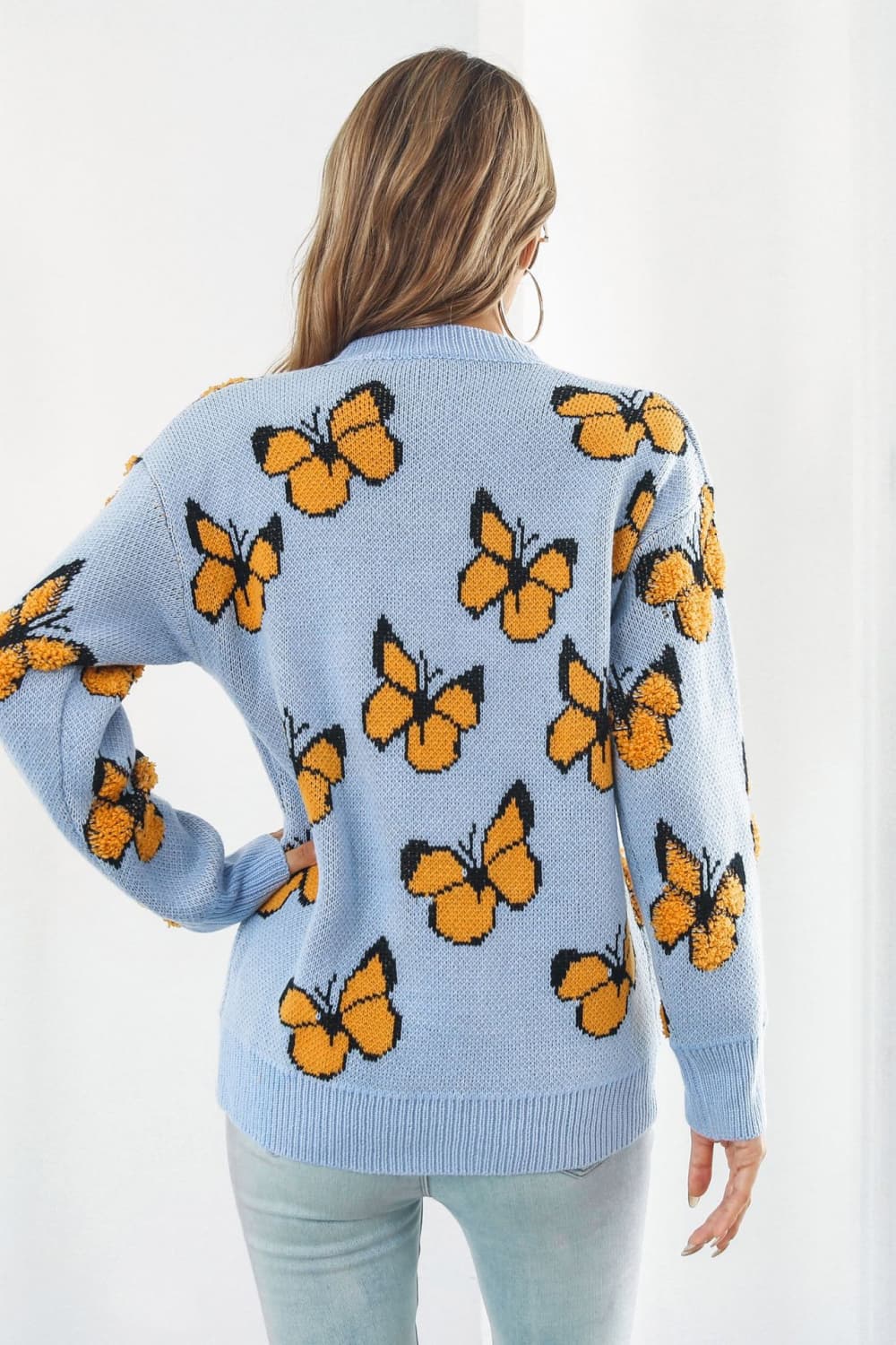 Pastel blue acrylic knit crewneck pullover with allover orange butterfly motif and textured details.