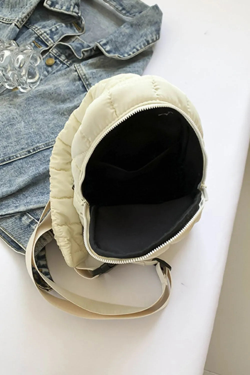Padded sling bag in ivory with quilted detail and top handle, open to show interior.