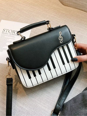 Black and white piano key crossbody bag with treble clef detail and top handle.