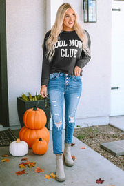 Charcoal crewneck sweatshirt with white "Cool Mom Club" graphic, styled with ripped jeans.