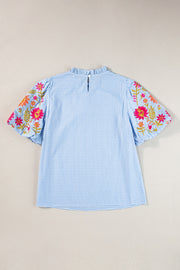 Light blue gingham blouse with embroidered floral puff sleeves and ruffled mock neck.