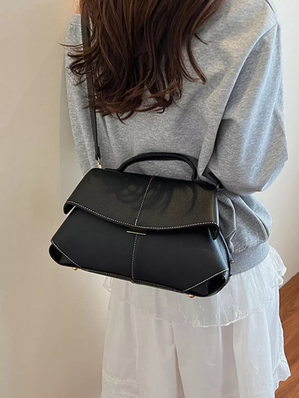 Black textured geometric flap shoulder bag with white contrast stitching and adjustable strap.