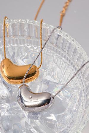 Gold and silver bean-shaped sculptural pendant necklaces on delicate chains.