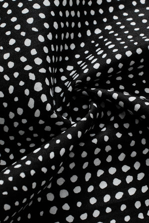 Black micro-dot blouse with puff sleeves and a swirling fabric detail.
