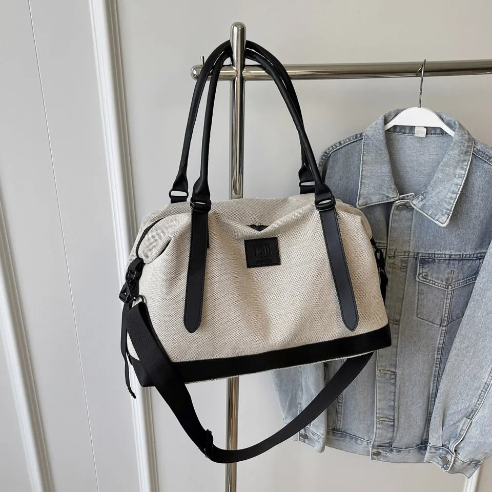 Canvas weekend holdall duffel bag in beige with black trim and straps, featuring a detachable shoulder strap.