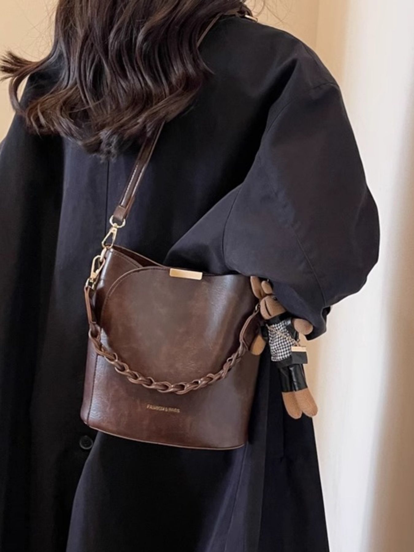 Brown braided bucket crossbody bag with chain detail and charm