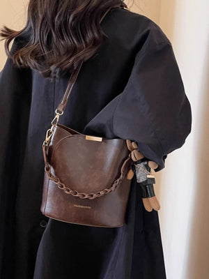 Brown braided bucket crossbody bag with chain detail and charm