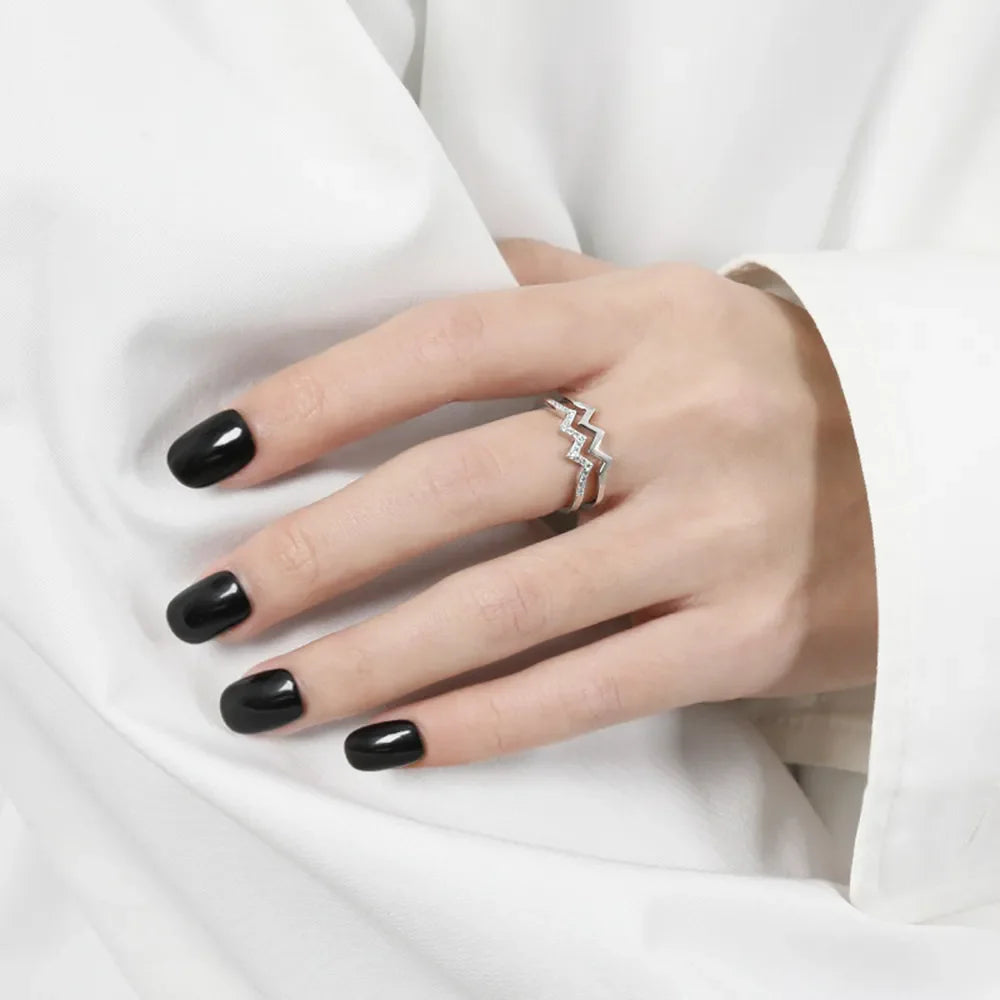 Silver zigzag split band ring with small stones on a hand with black nails.
