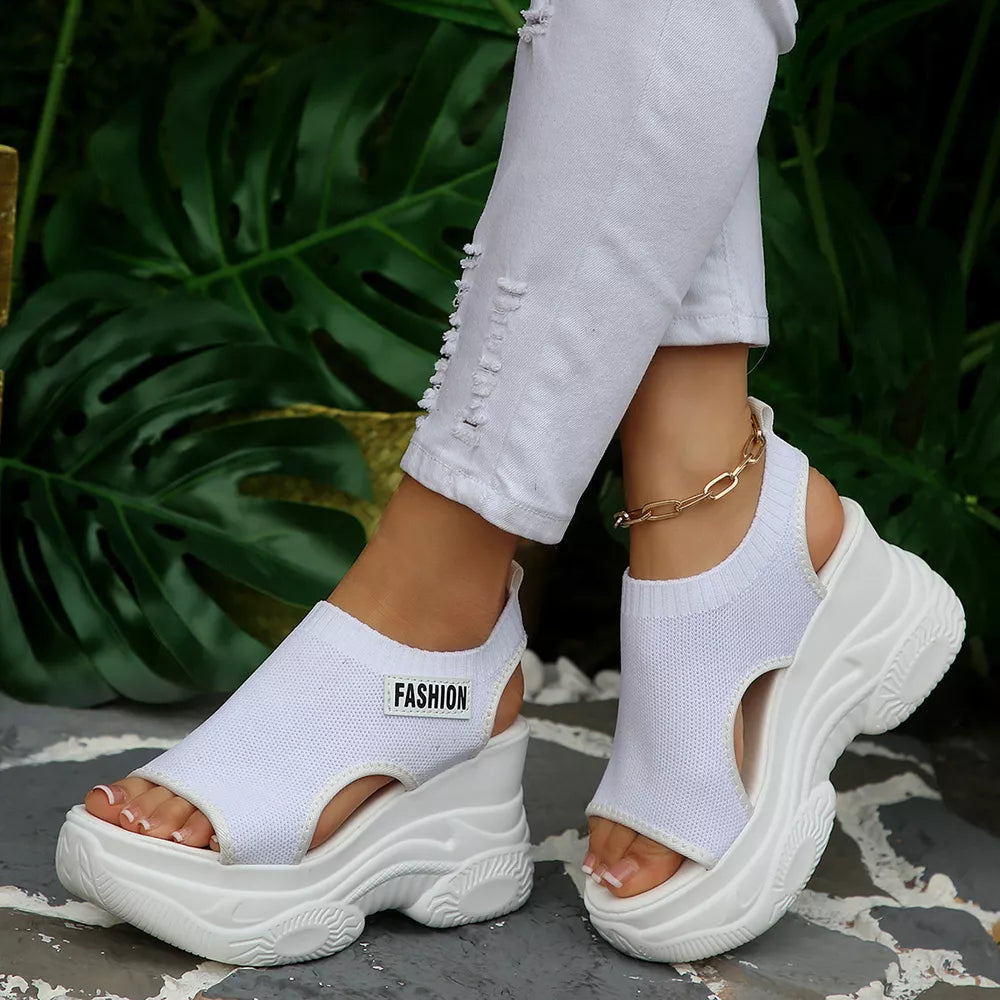 Fashion-forward white open-toe wedge sandals with chunky sole and ankle strap detail.