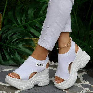 Fashion-forward white open-toe wedge sandals with chunky sole and ankle strap detail.
