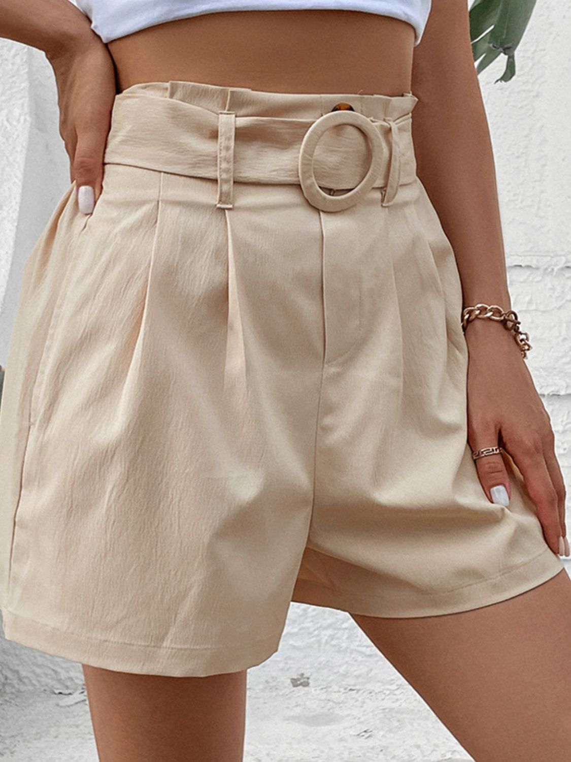 Cream high-waisted pleated shorts with a fabric belt and circular buckle.
