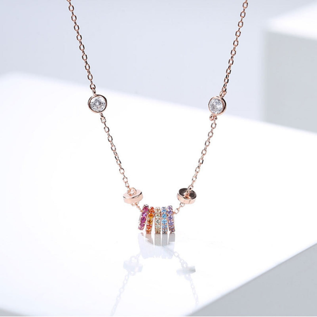 Rose gold necklace with a fine chain, featuring a cluster of colorful crystal rings and two clear crystal accents.