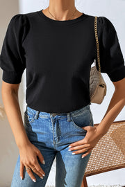 Black knit sweater with puff sleeves and crew neck, styled with jeans.