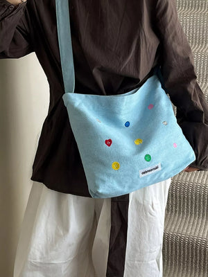 Light blue denim crossbody bag with colorful button embroidery and adjustable strap