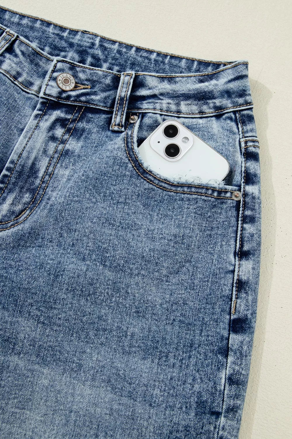 Cuffed mid-rise relaxed fit jeans in distressed blue denim with a phone in the pocket.