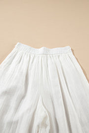 White pleated linen palazzo trousers with elastic waistband and wide leg