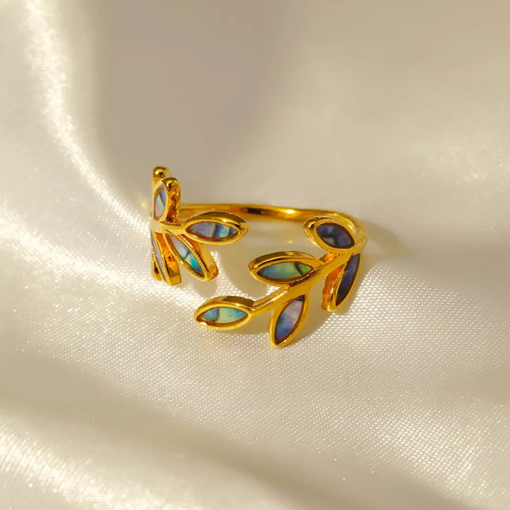 Gold bypass ring with leaf design and iridescent blue accents on white satin.