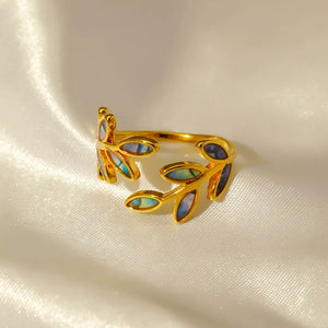 Gold bypass ring with leaf design and iridescent blue accents on white satin.