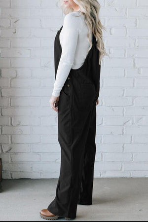 Black corduroy wide-leg overalls with button details and pockets, styled with a white long-sleeve shirt.
