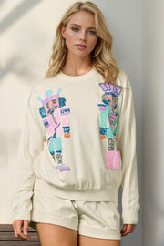 Cream knit crewneck sweater with colorful sequin nutcracker appliqué, long sleeves, 100% polyester.
