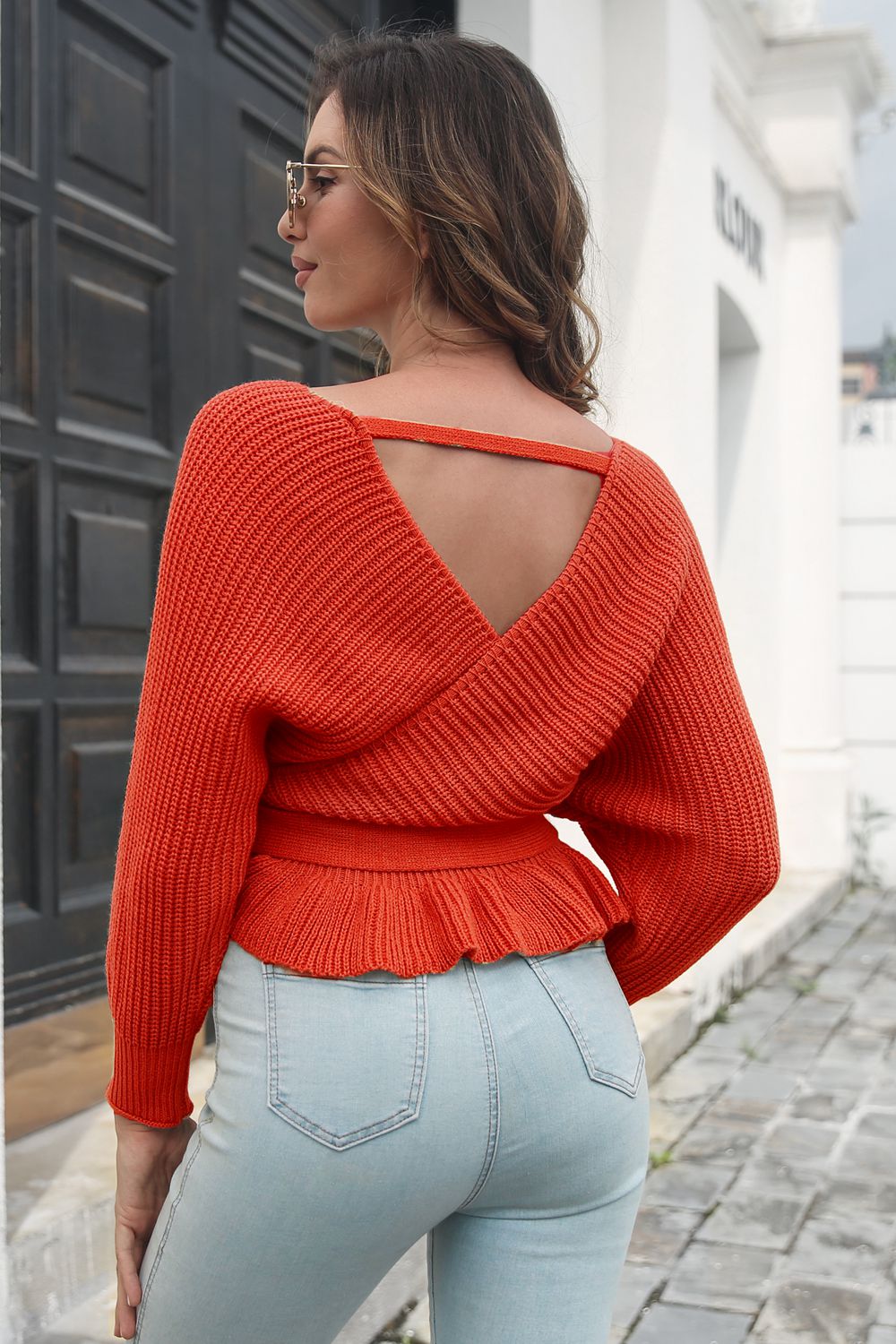 Orange-red acrylic wrap sweater with open back detail and peplum hem