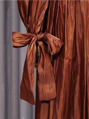 Brown ruched maternity maxi dress with a tied bow detail on the sleeve.
