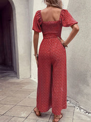 Red floral smocked bodice jumpsuit with puff sleeves and wide legs.