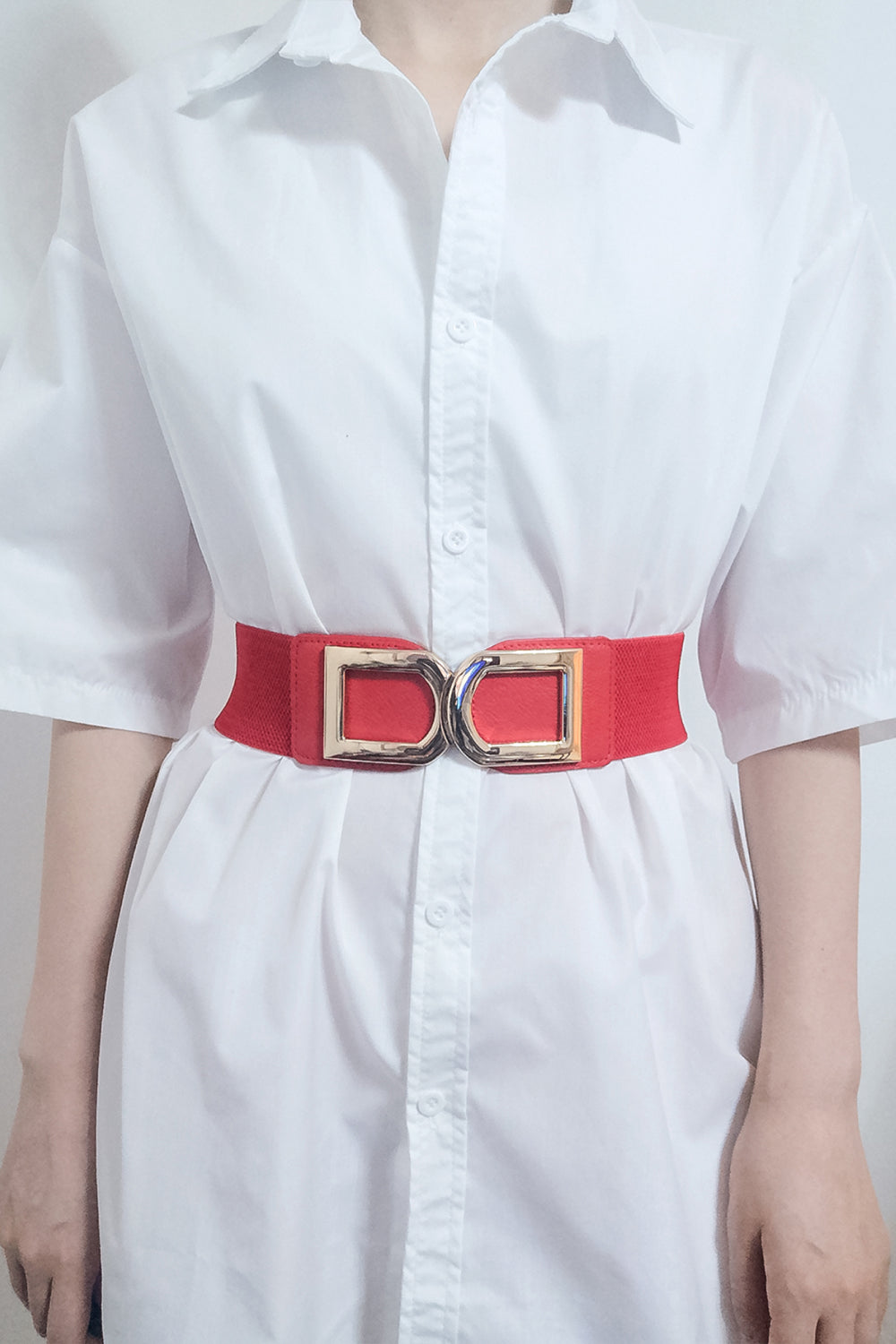 Red elastic belt with double gold buckle detail worn over a white shirt.