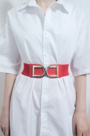 Red elastic belt with double gold buckle detail worn over a white shirt.