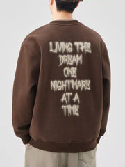 Brown oversized crew-neck sweatshirt with "Living the Dream One Nightmare at a Time" graphic on back