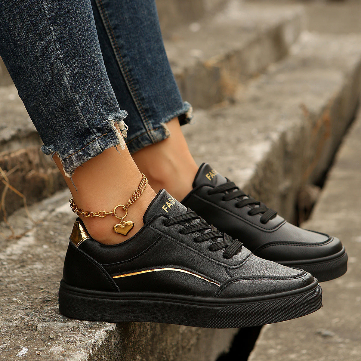 Black lace-up casual sneakers with gold accents and a heart charm anklet.