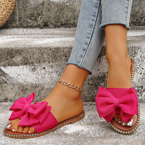 Fuchsia pink bowknot slide sandals with a gold chain anklet.