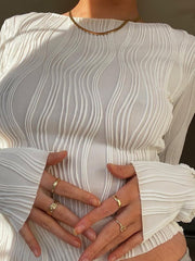 White textured fitted blouse with long sleeves and asymmetrical hem, styled with gold rings.