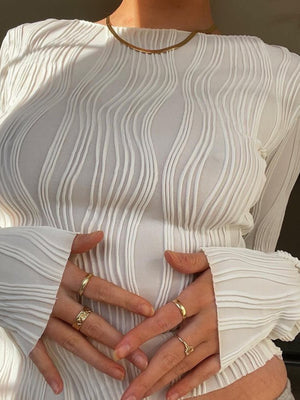 White textured fitted blouse with long sleeves and asymmetrical hem, styled with gold rings.