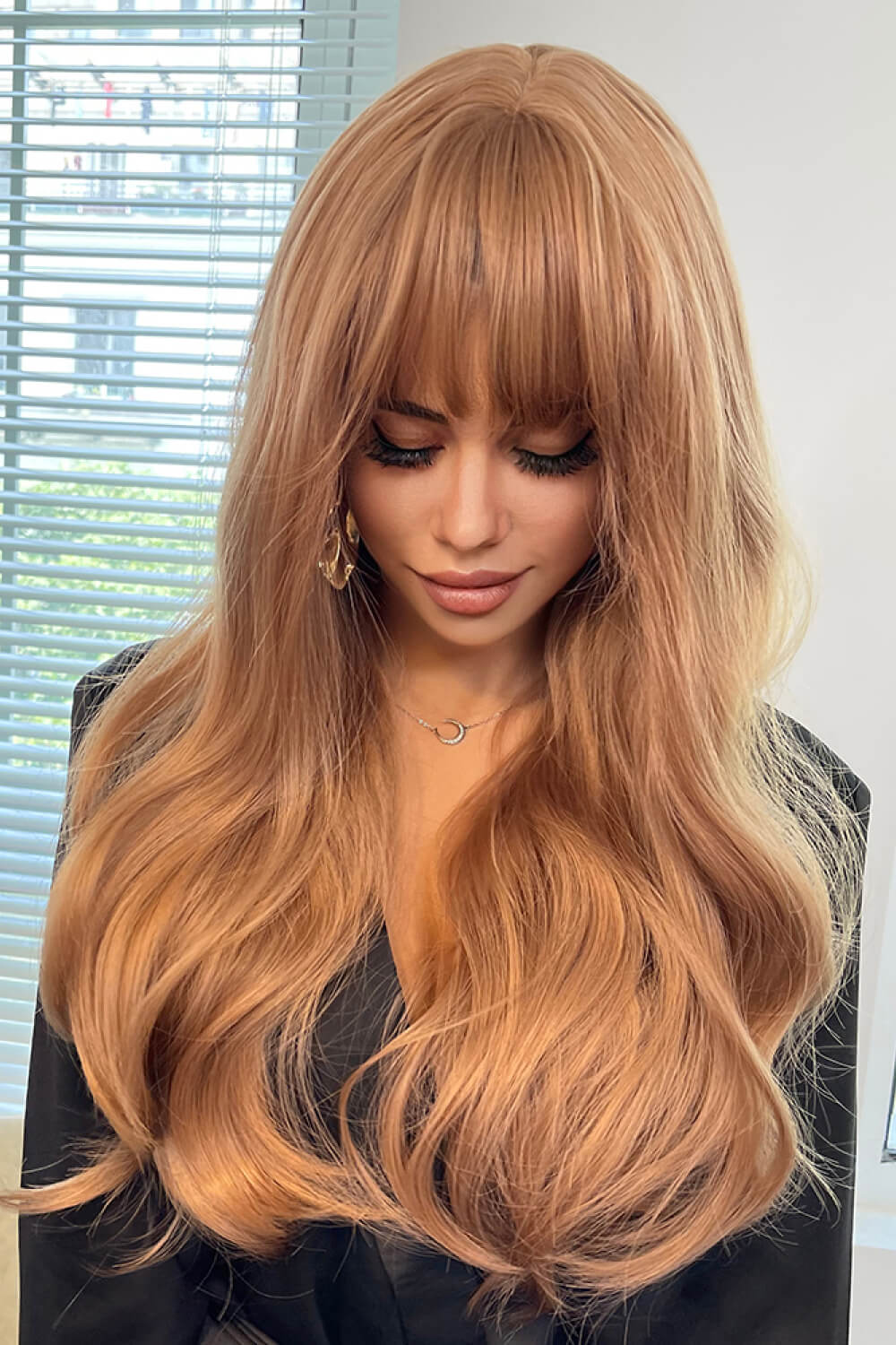 Strawberry blonde wig with bangs and loose waves, styled with a black top.