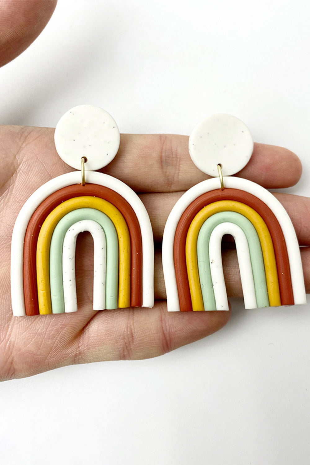 Rainbow arch clay earrings in white, rust, yellow, mint green, and white.