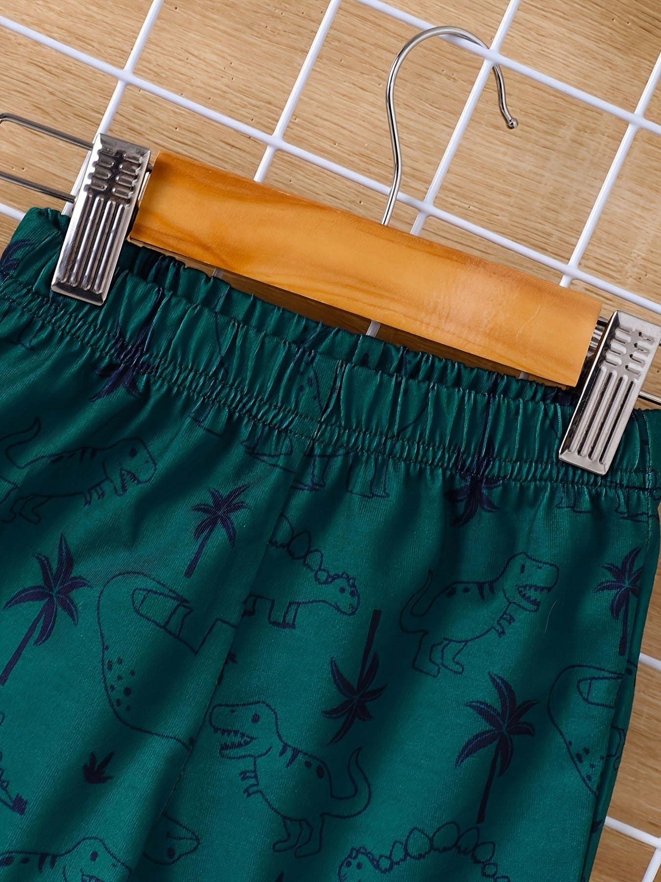 Green baby shorts with elastic waist and allover dinosaur and palm tree print.