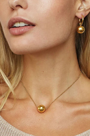 Gold orb pendant necklace on a delicate chain, styled with matching hoop earrings.
