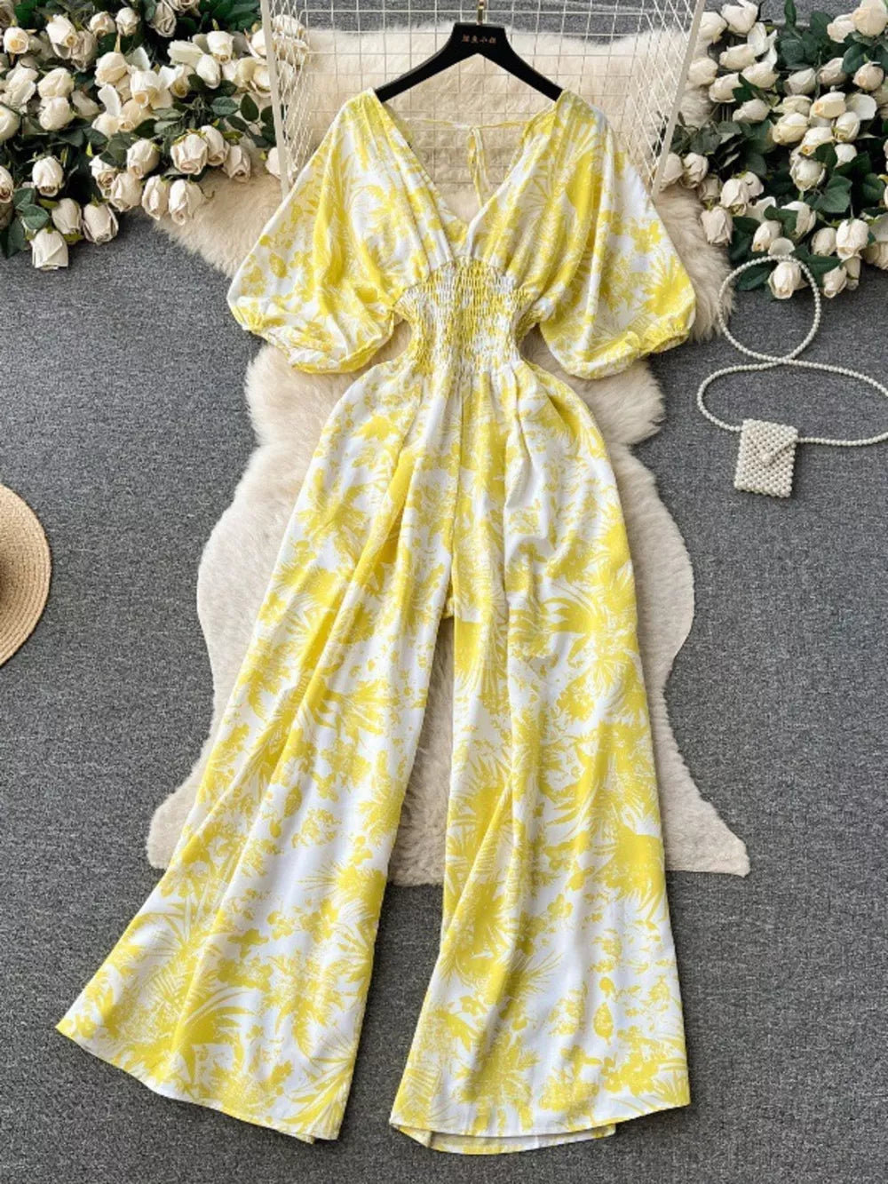 Yellow tropical print smocked wide-leg romper with V-neck and puff sleeves.