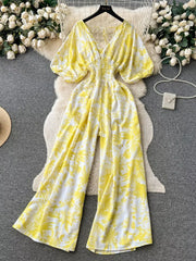 Yellow tropical print smocked wide-leg romper with V-neck and puff sleeves.