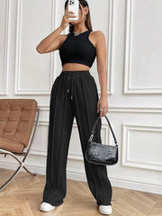 Black pleated wide-leg lounge trousers with drawstring waist and white sneakers.