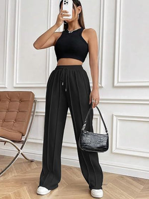 Black pleated wide-leg lounge trousers with drawstring waist and white sneakers.